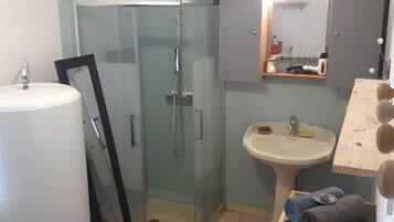 Une salle de bain avec une douche à parois de verre, un lavabo avec un miroir au-dessus et une serviette posée sur une table.