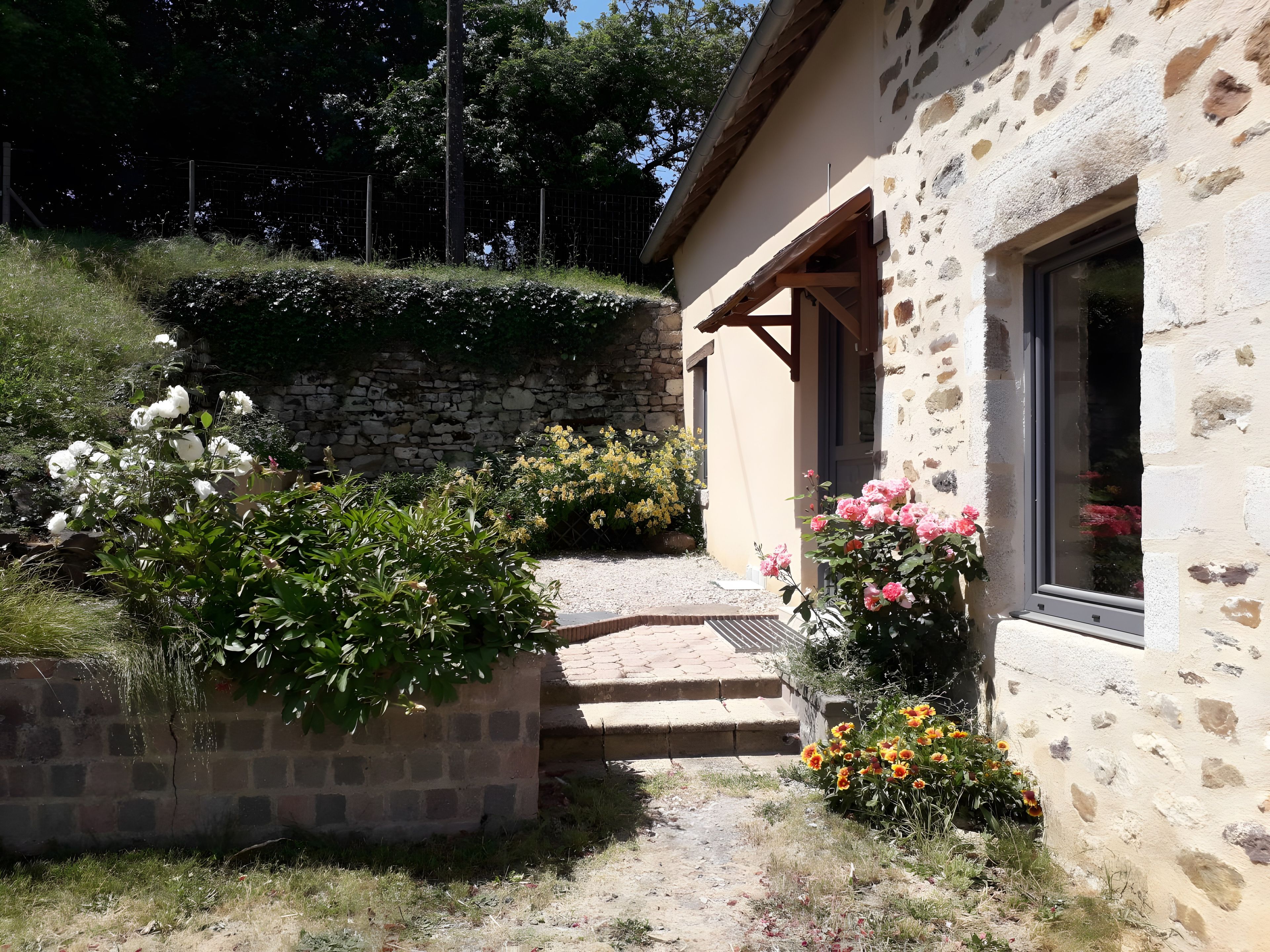 Un bâtiment en pierre avec une entrée donnant sur un jardin, des marches menant à une porte et un mur en pierre.