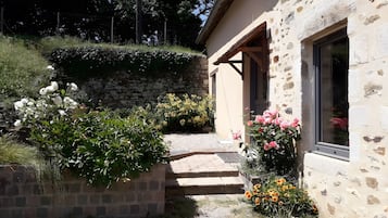 Un bâtiment en pierre avec une entrée donnant sur un jardin, des marches menant à une porte et un mur en pierre.