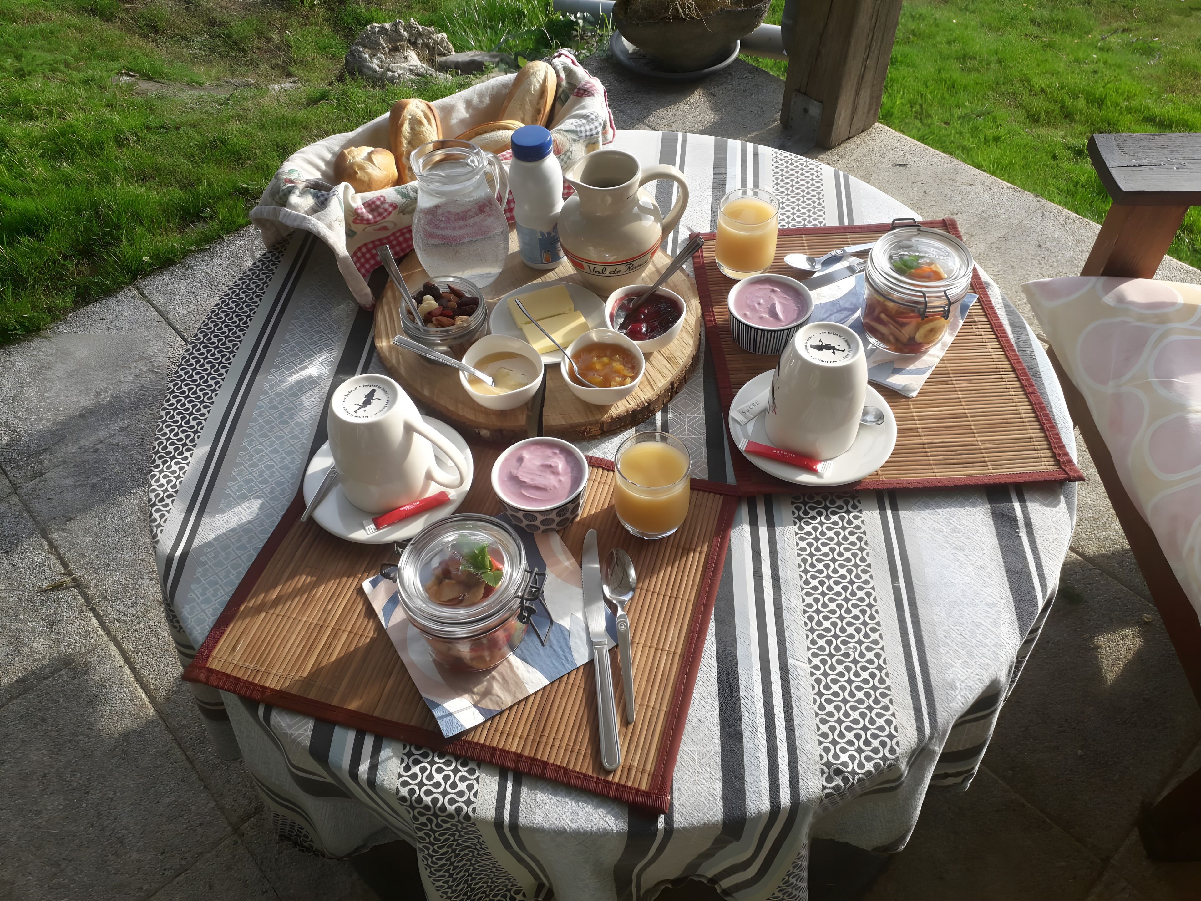 An outdoor breakfast setup with a variety of food items, beverages, and utensils on a round table.
