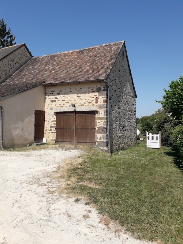 A stone building with a tiled roof, a wooden door, and a gravel driveway.