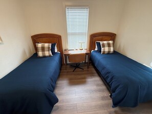 Una habitación con dos camas individuales, una mesita y una silla.