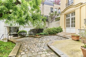 A courtyard with stone paving, a staircase, and potted plants. - Apartment Le Marais/ Place des Vosges (Paris)