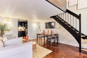 A modern living room with a dining area, a staircase, and a kitchen in the background. - Apartment Le Marais/ Place des Vosges (Paris)