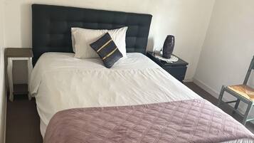 Een slaapkamer met een bed, een nachtkastje, een stoel en een schilderij aan de muur.