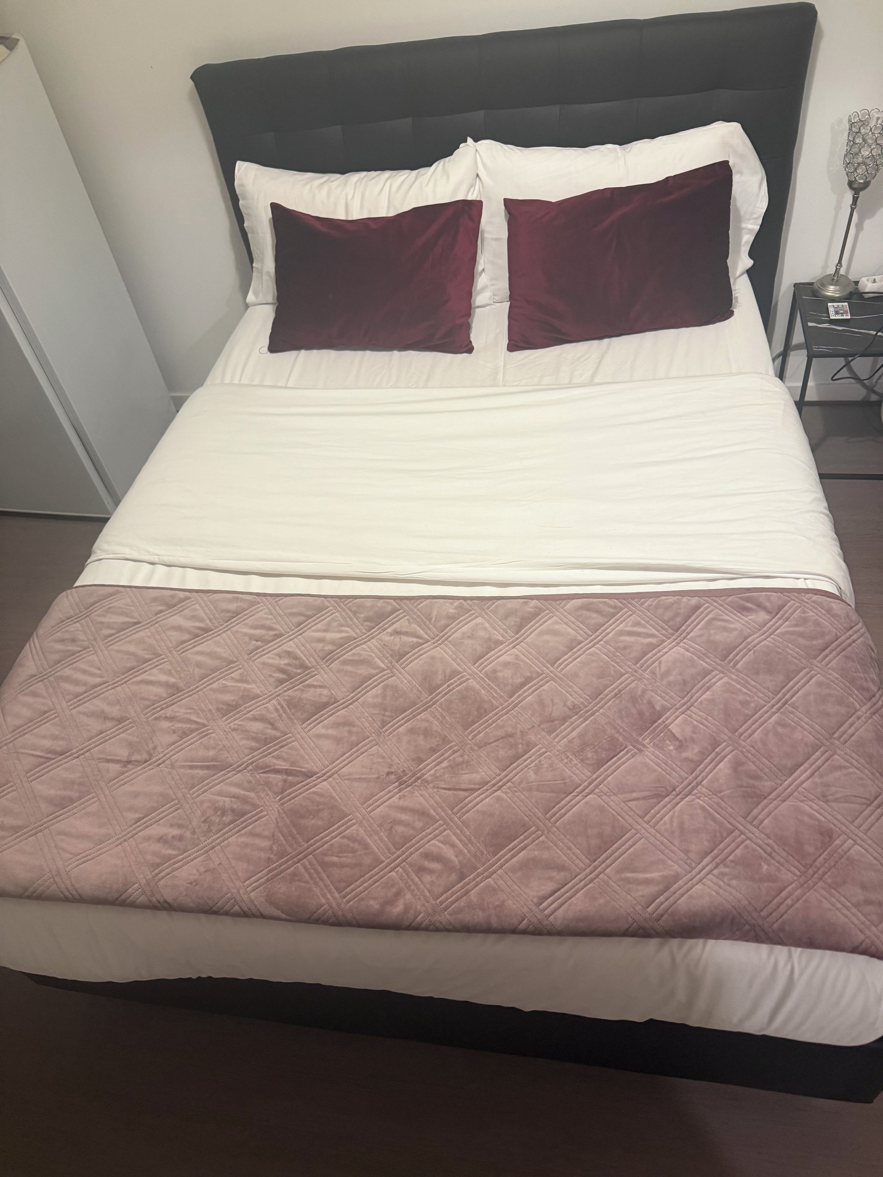 Een bed met een gewatteerde spreideken, een donker hoofdbord en twee kussens.