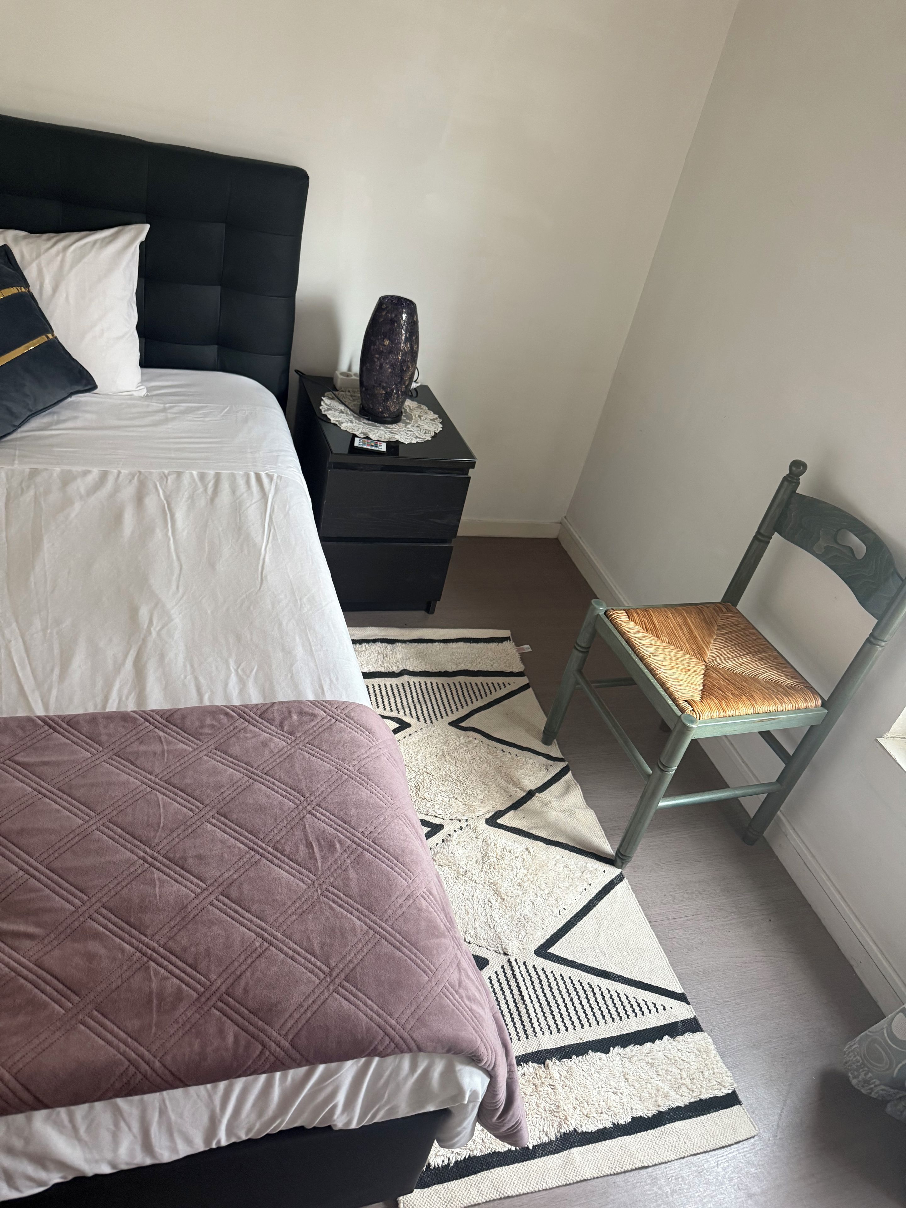 Een slaapkamer met een bed, een nachtkastje, een stoel en een vloerkleed.