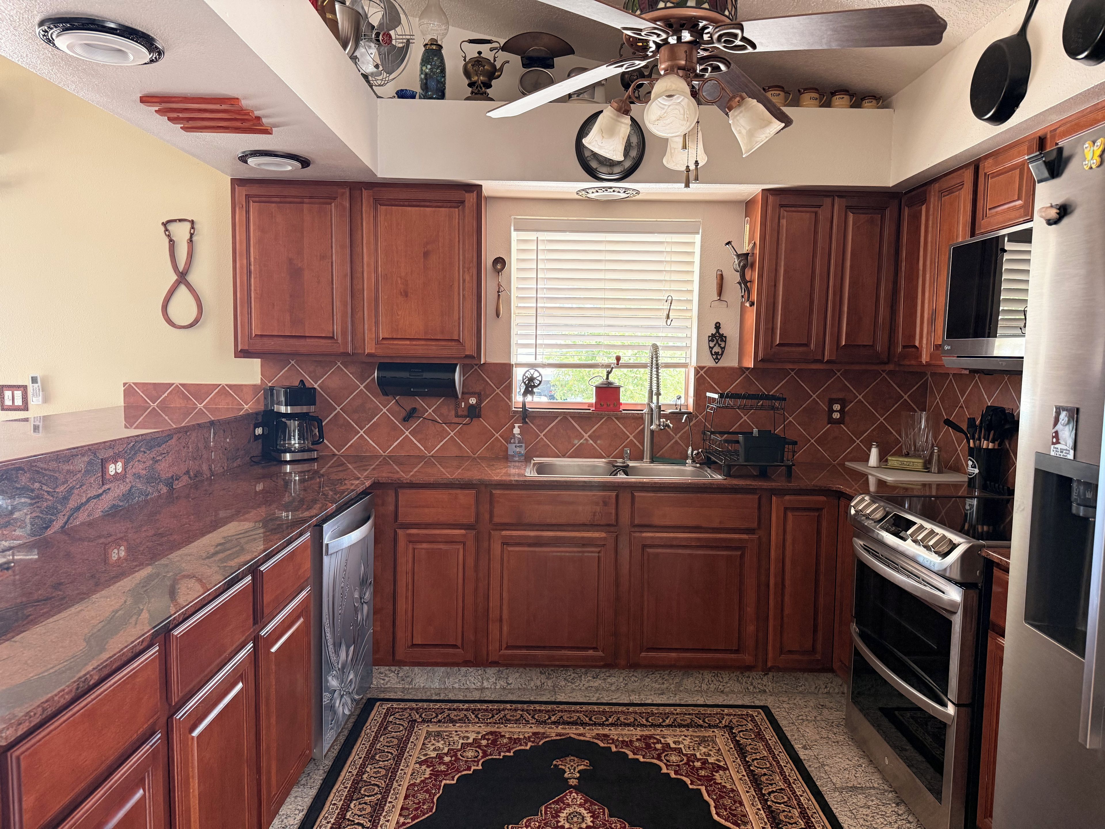A kitchen with wooden cabinets, a marble countertop, a built-in oven, and a ceiling fan.