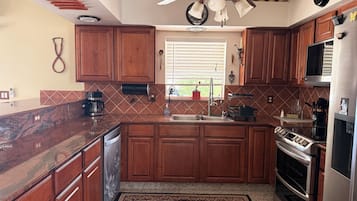 A kitchen with wooden cabinets, a marble countertop, a built-in oven, and a ceiling fan.