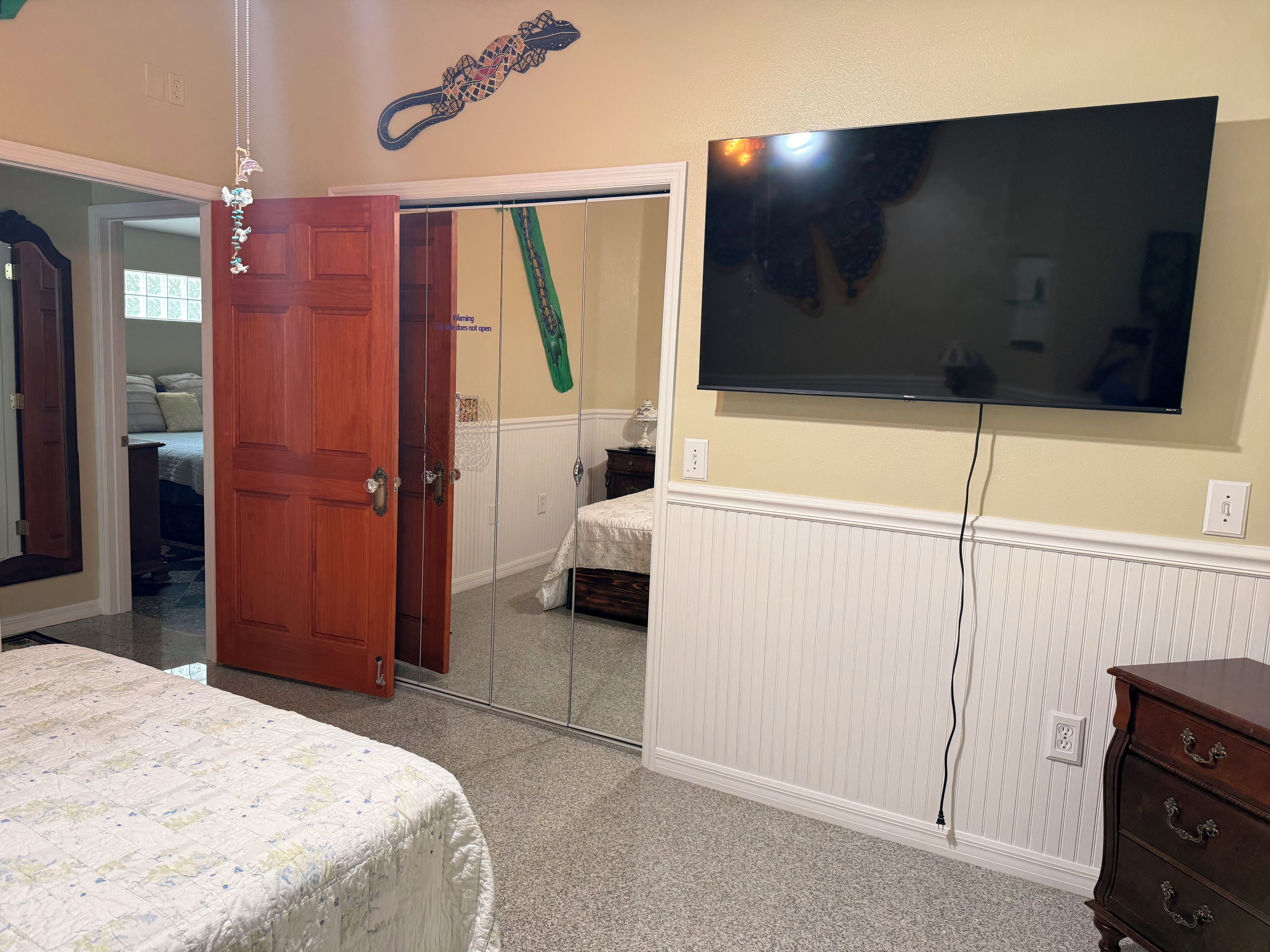 A bedroom with a bed, a dresser, a television mounted on the wall, and a door leading to another room.