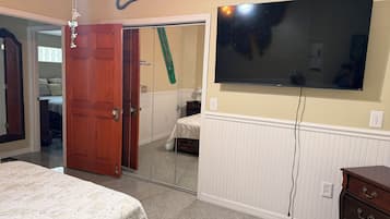 A bedroom with a bed, a dresser, a television mounted on the wall, and a door leading to another room.