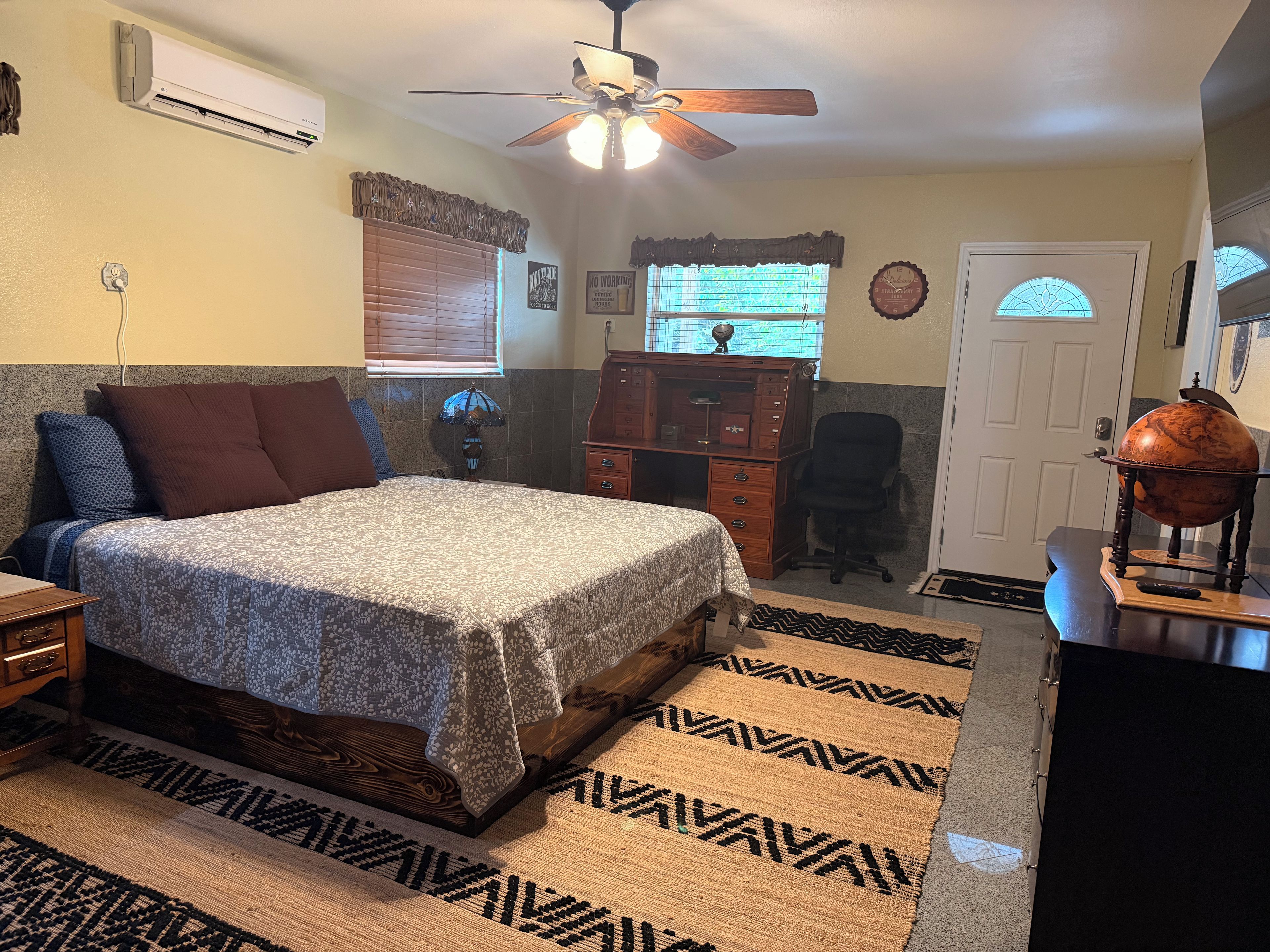 A bedroom with a bed, a desk, a globe, and a window with blinds.