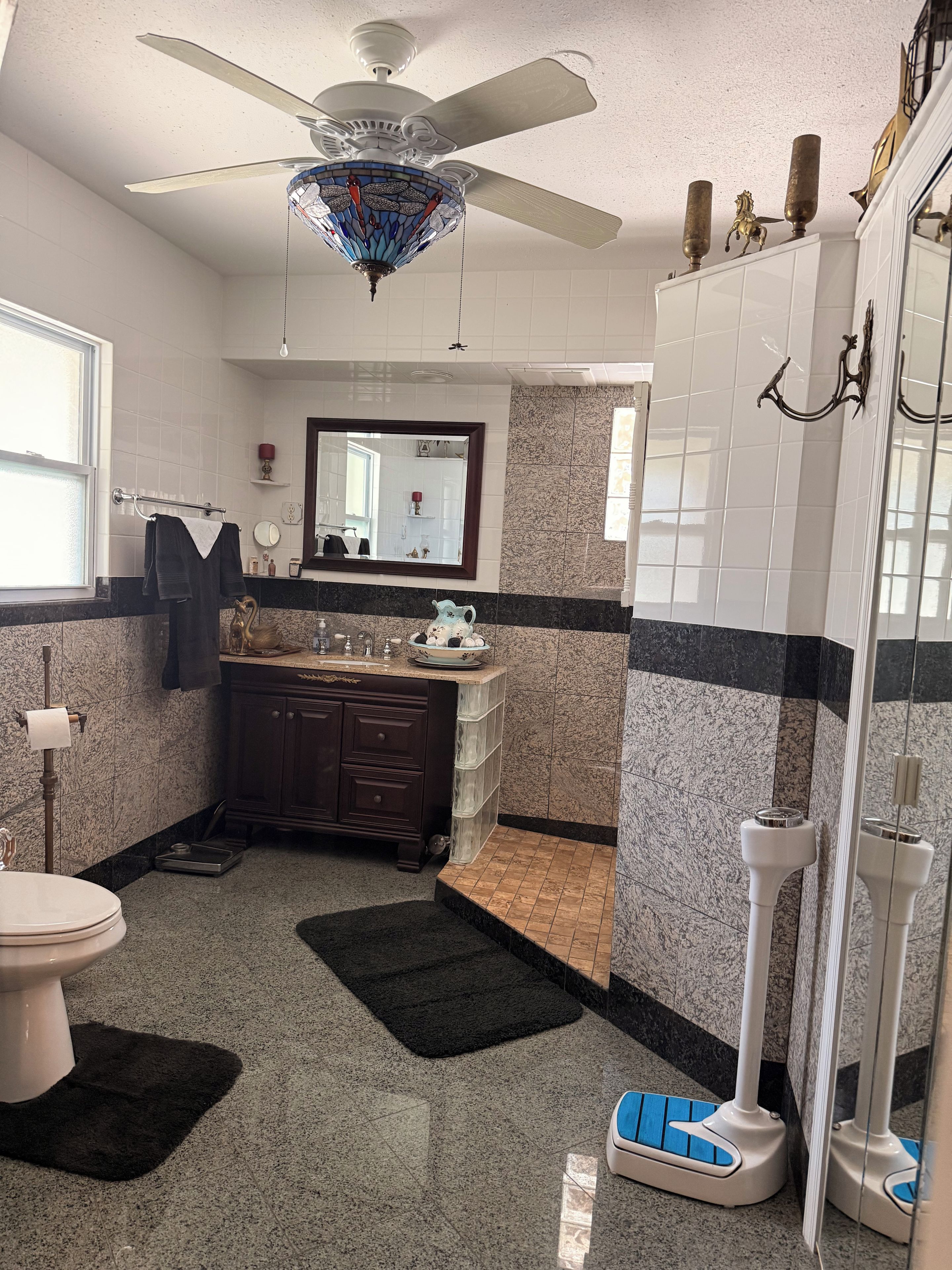 Een badkamer met toilet, wastafel, badkamermeubel, spiegel, plafondventilator en douche.