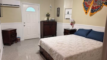 Een slaapkamer met een bed, een dressoir, nachtkastje, lamp en een decoratieve vlinder.