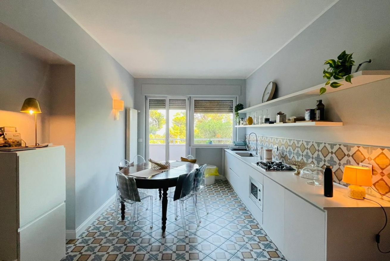 Cocina compacta con una mesa de comedor, sillas, refrigerador, pileta y ventana con vista a follaje.