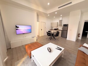 A modern living space with a flat-screen TV, a dining area with a white table, and a kitchen with stainless steel appliances. - Walk to Beach Modern 1-Bed Apt CasaAmarilla205 (Oranjestad)