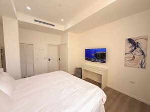 Ein Schlafzimmer mit einem Bett, einem an der Wand montierten Fernseher, einem Schreibtisch und einem Gemälde.