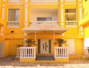 Ein gelbes Gebäude mit einem Schild, auf dem 'Casa Amarilla Boutique Suites' steht, und einem überdachten Eingang mit einer weißen Balustrade.