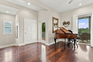 A spacious room with hardwood flooring, a grand piano, a large mirror, and a sliding glass door leading to a balcony. - Pet-Friendly Canal Retreat  Pool & Balconies (Bonita Springs)