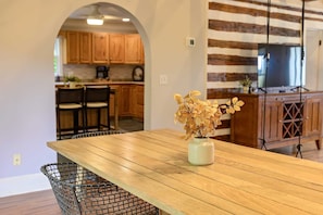 A wooden dining table with a vase of dried flowers, a metal basket, and a kitchen area with wooden cabinets and a stone wall. - Ridgeview Home with Hot Tub in Lookout Valley (Chattanooga)