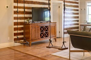 A room with a wooden floor, a wooden cabinet with a TV on top, and a swing chair. - Ridgeview Home with Hot Tub in Lookout Valley (Chattanooga)