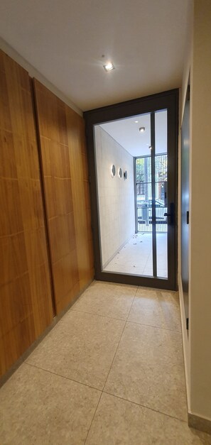 A room with a tiled floor, a wooden panel wall, and a large sliding glass door leading to an outdoor area. - Bright apartment in Palermo Soho (Buenos Aires)