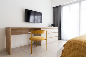 A modern hotel room with a wooden desk, a flat-screen TV mounted above it, a yellow chair, a bed with a patterned blanket, and a window with sheer curtains. - Bright Apartment in Palermo Soho (Buenos Aires)