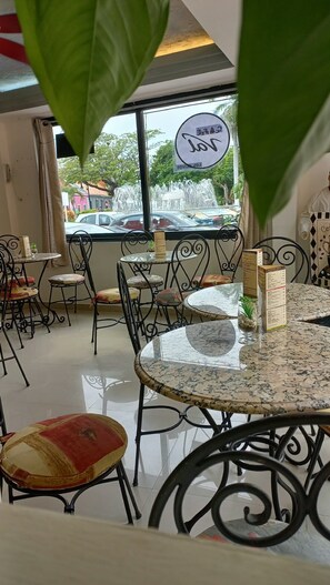 An indoor seating area with round tables and chairs, a view of a fountain outside, and a sign indicating a COVID-19 measure.