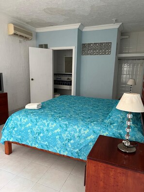 Un dormitorio con cama, lámpara de noche, armario y un baño visible a través de una puerta abierta.