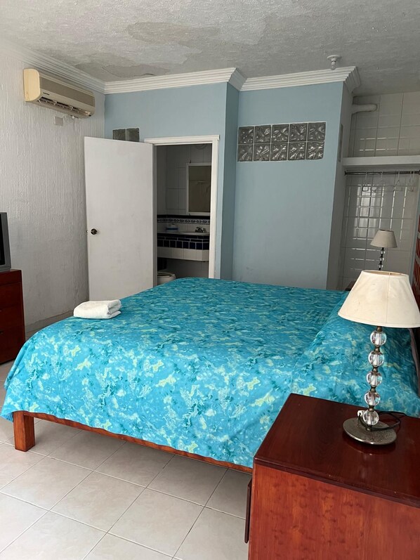 A bedroom with a bed, a bedside lamp, a wardrobe, and a bathroom visible through an open door.