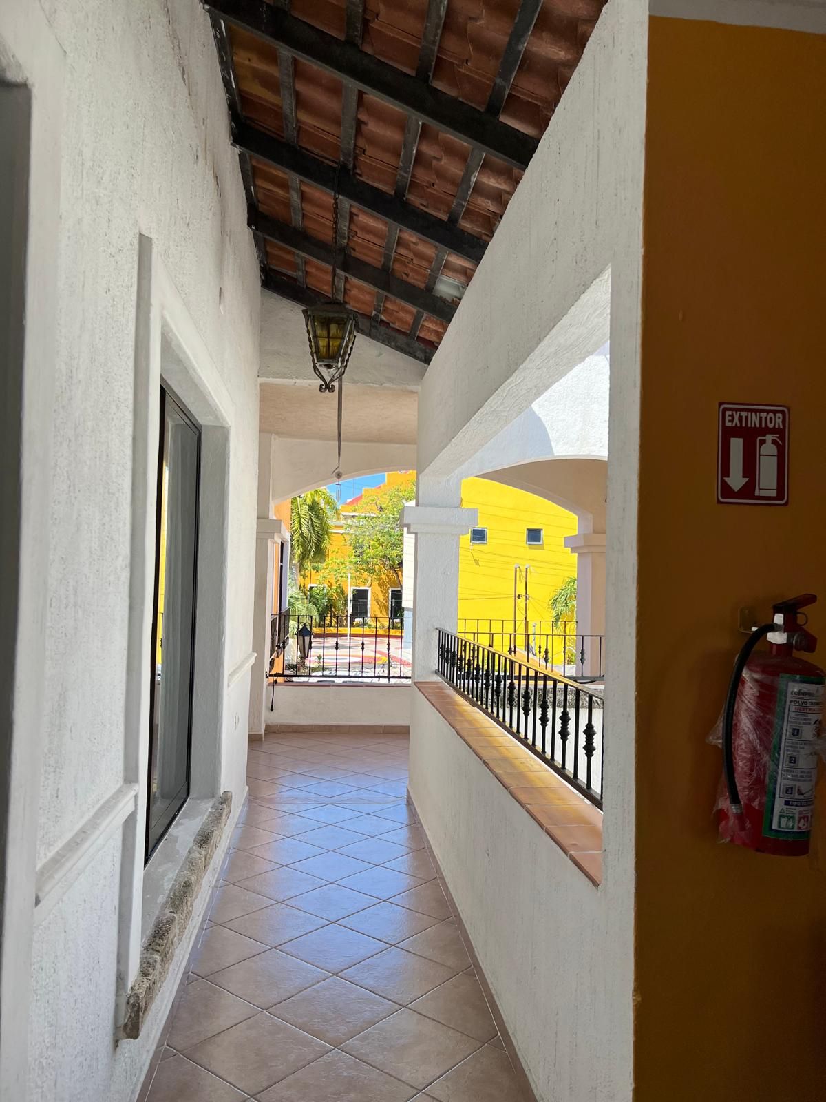 Un pasillo con piso de baldosas, un extintor de incendios en la pared y un letrero que indica una salida.
