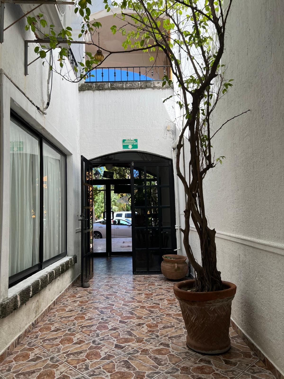 A corridor with a tiled floor leading to a black door with a green emergency exit sign above it.