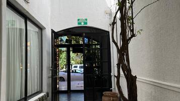 A corridor with a tiled floor leading to a black door with a green emergency exit sign above it.