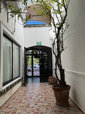 A corridor with a tiled floor leading to a black door with a green emergency exit sign above it.
