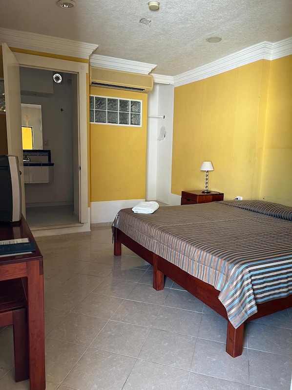 A hotel room with a bed, a desk, a lamp, and a bathroom visible through an open door.