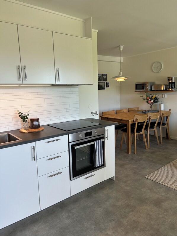 A modern kitchen with white cabinetry, a built-in oven, and a dining area with a wooden table and chairs.