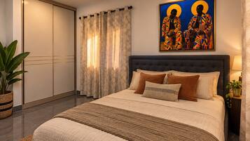 A bedroom with a large bed, a ceiling fan, a painting on the wall, and a window with curtains.