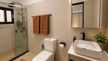 Un bagno moderno con cabina doccia in vetro, un WC, un lavandino e uno specchio.