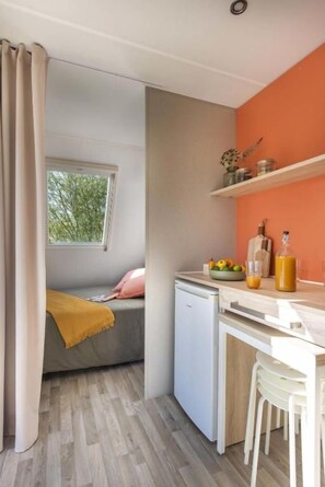 Una cocina compacta con ventana, un refrigerador pequeño, un lavamanos y una encimera con un frutero y una botella.