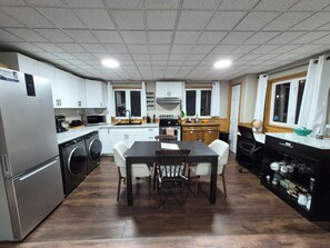 A compact kitchen with a built-in washing machine, a dining area with a table and chairs, and wooden cabinets.