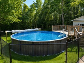 An above-ground swimming pool surrounded by a wooden deck and a chain-link fence.