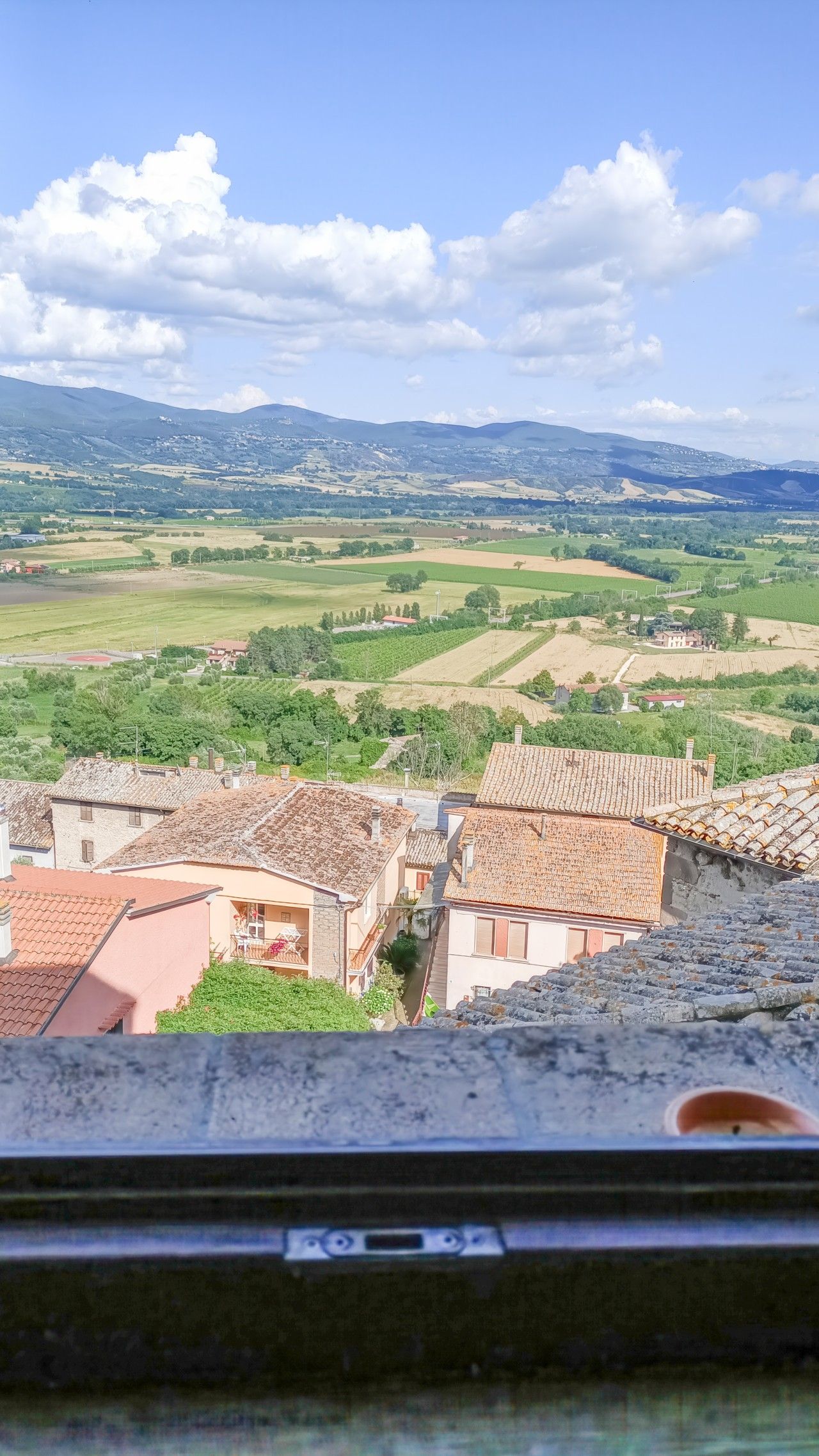 Vista di una città con edifici dalle tegole color terracotta e un paesaggio verdeggiante.