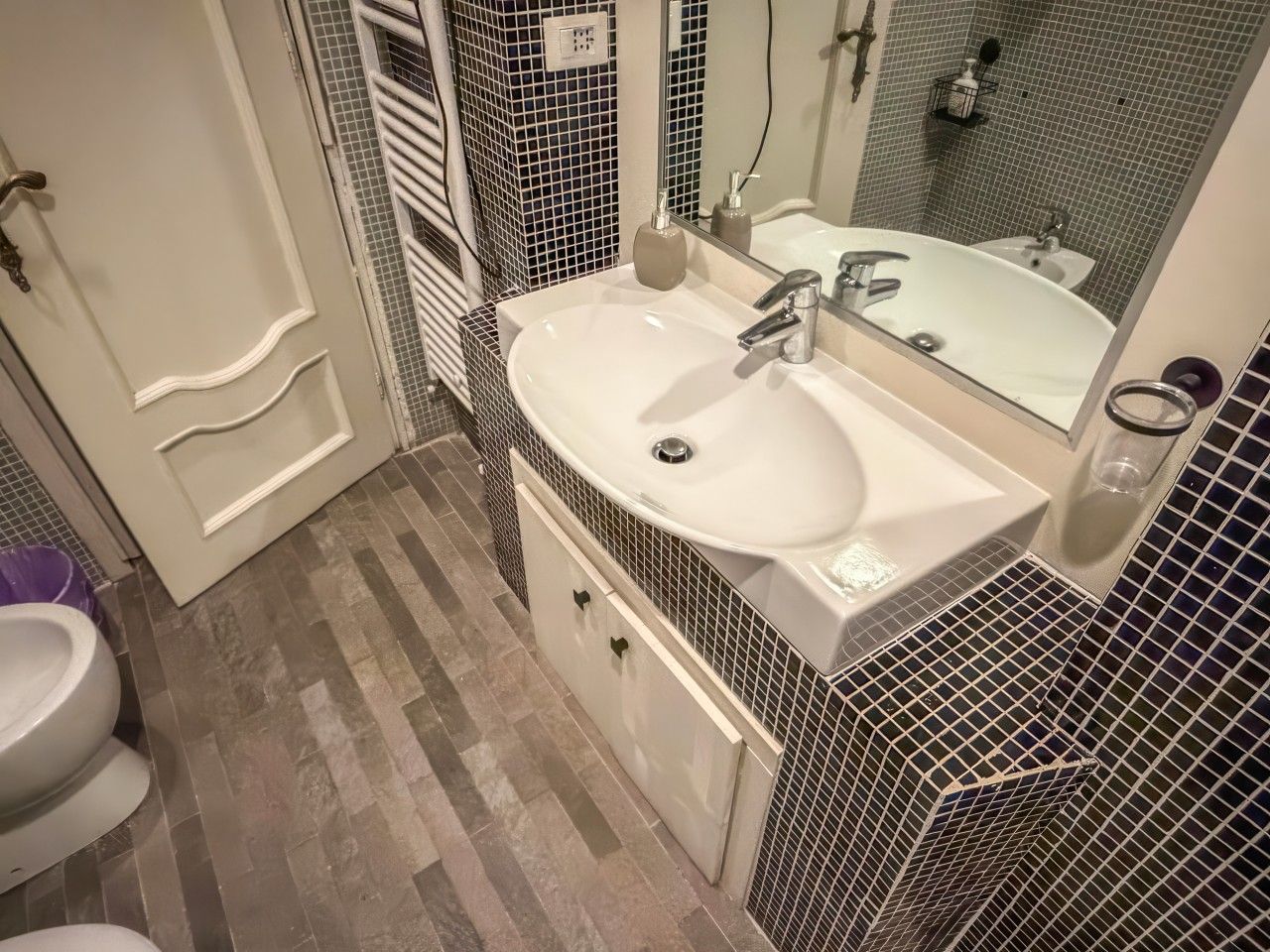 A bathroom with a white sink, a mirror, a toilet, and a shower area.