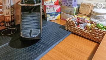 A kitchen counter with a coffee maker, boxes of tea, a jar of flour, and a basket of snacks.