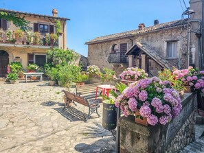 A cobblestone courtyard with benches, potted plants, and a building with a balcony. - Domus Claudia - Castiglione in Teverina (Castiglione In Teverina)