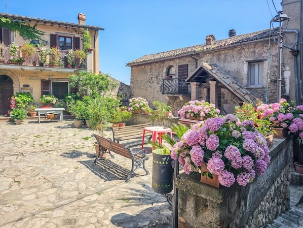 A cobblestone courtyard with benches, potted plants, and a building with a balcony. - Domus Claudia - Castiglione in Teverina (Castiglione In Teverina)