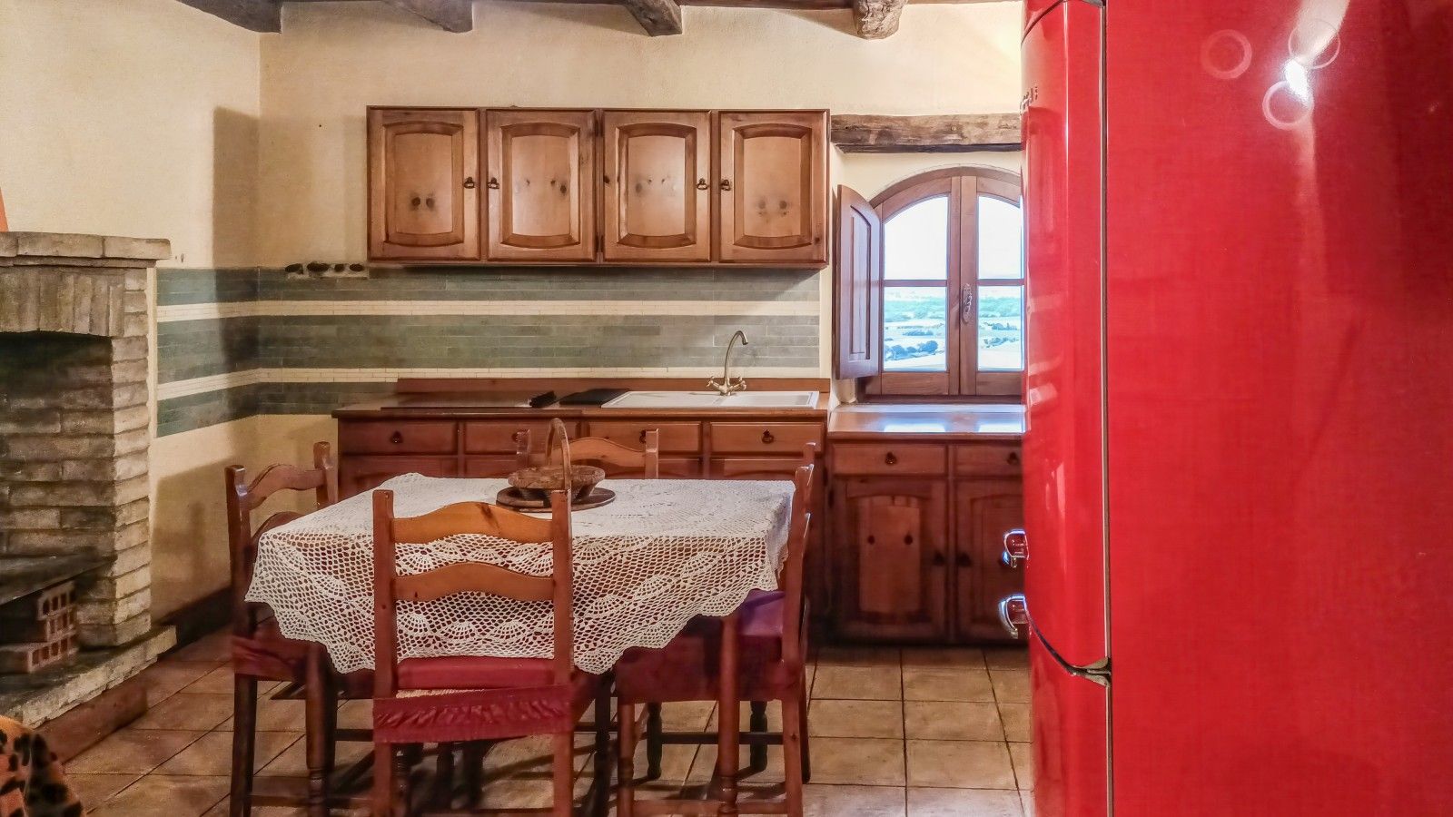 A kitchen with wooden cabinets, a red refrigerator, and a table with a lace tablecloth.