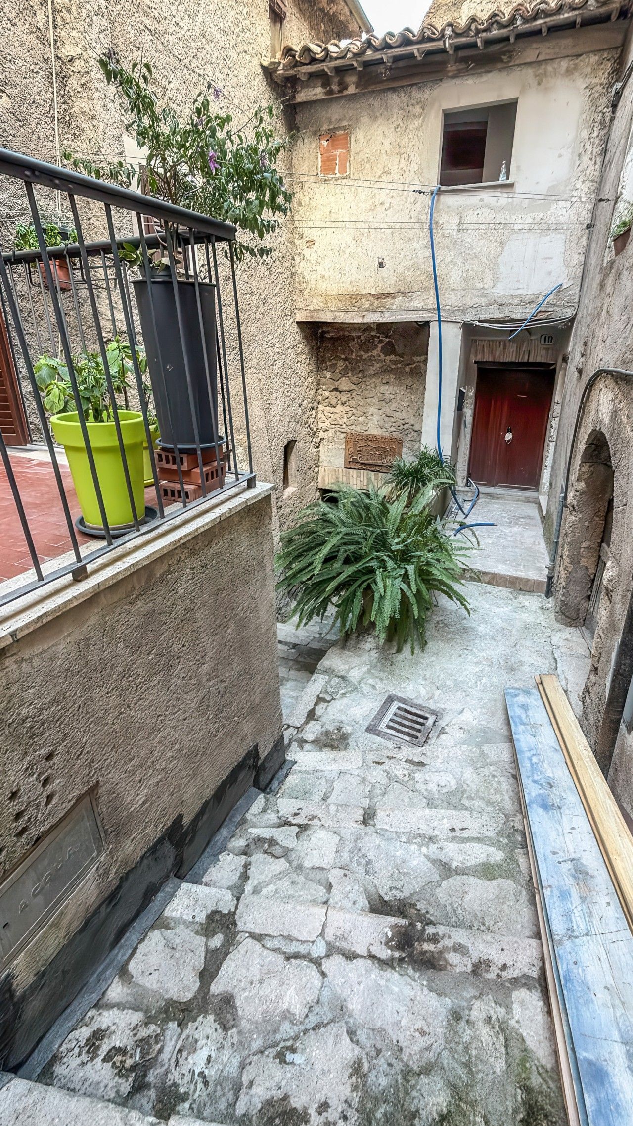 Une cour avec un sol en pierre, des plantes en pot et une rambarde en métal.