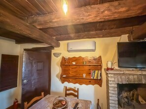 Une pièce chaleureuse avec un plafond en bois, une cheminée, une télévision et une étagère en bois où sont posés des livres et des verres.
