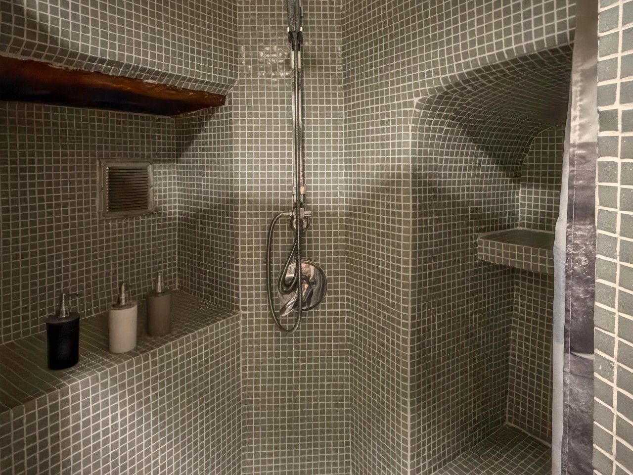 Une cabine de douche carrelée, dotée d’un pommeau de douche, d’une étagère pour les articles de toilette et d’une petite fenêtre.